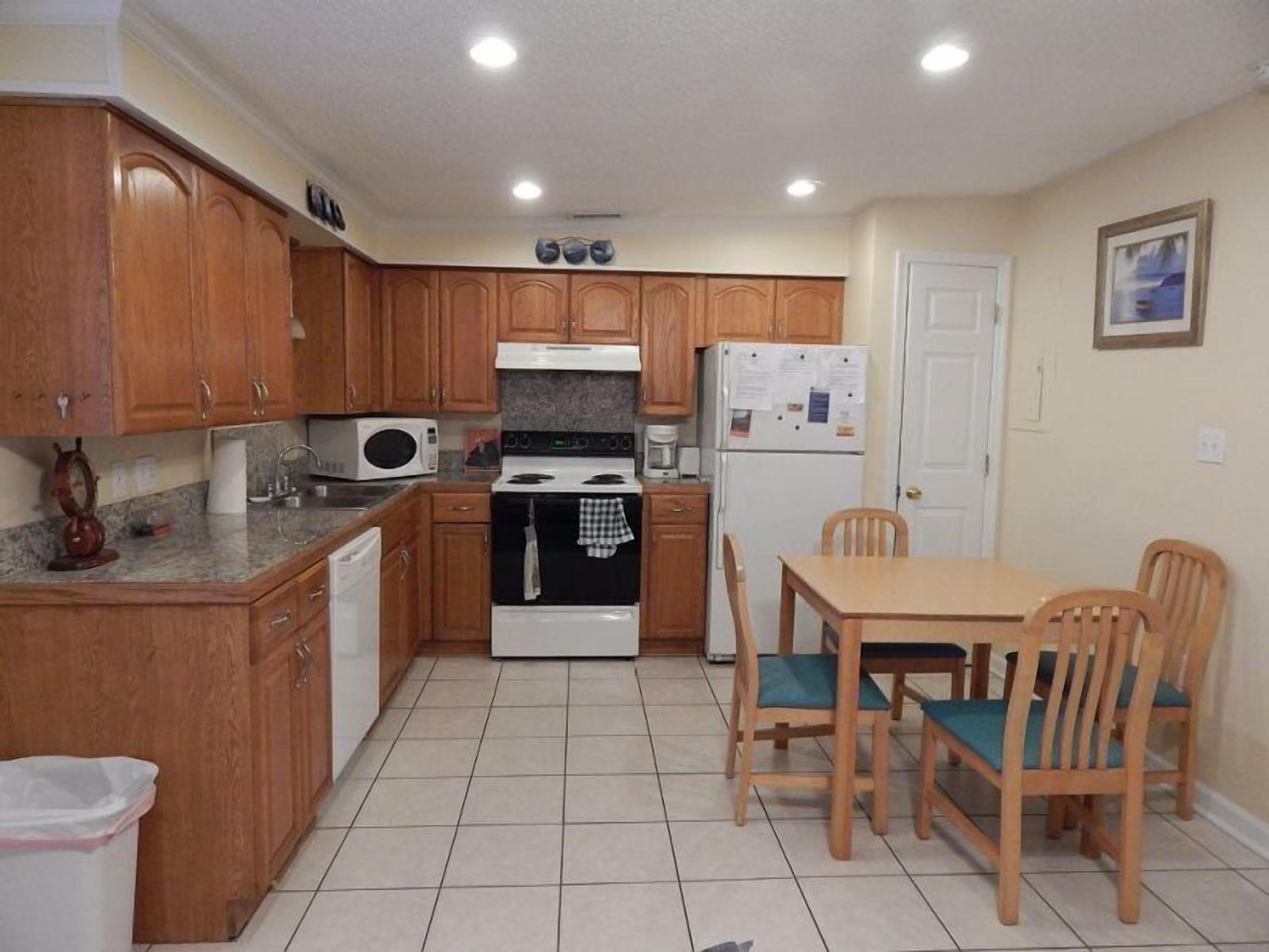 Una cocina compacta con armarios de madera, microondas, estufa, refrigerador y una mesa de comedor con sillas.