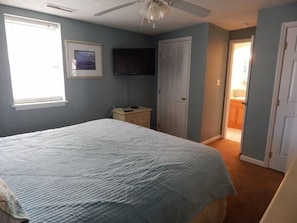 Um quarto com uma cama, uma mesa de cabeceira, uma televisão e uma porta que dá para um banheiro.