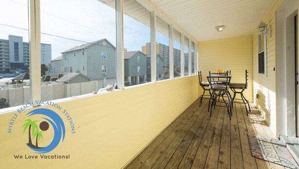 Un balcon fermé avec une table et des chaises, de grandes fenêtres et une vue sur les bâtiments.