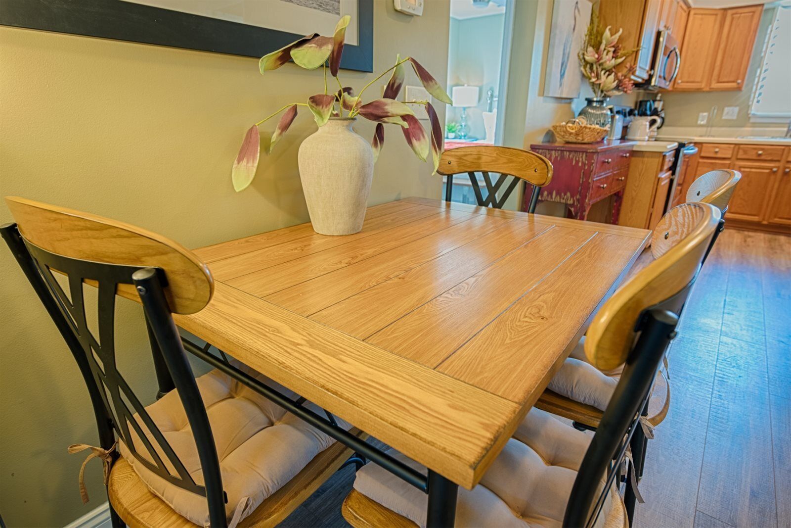 Une table à manger avec quatre chaises, un vase rempli de fleurs et, au fond, des meubles en bois.