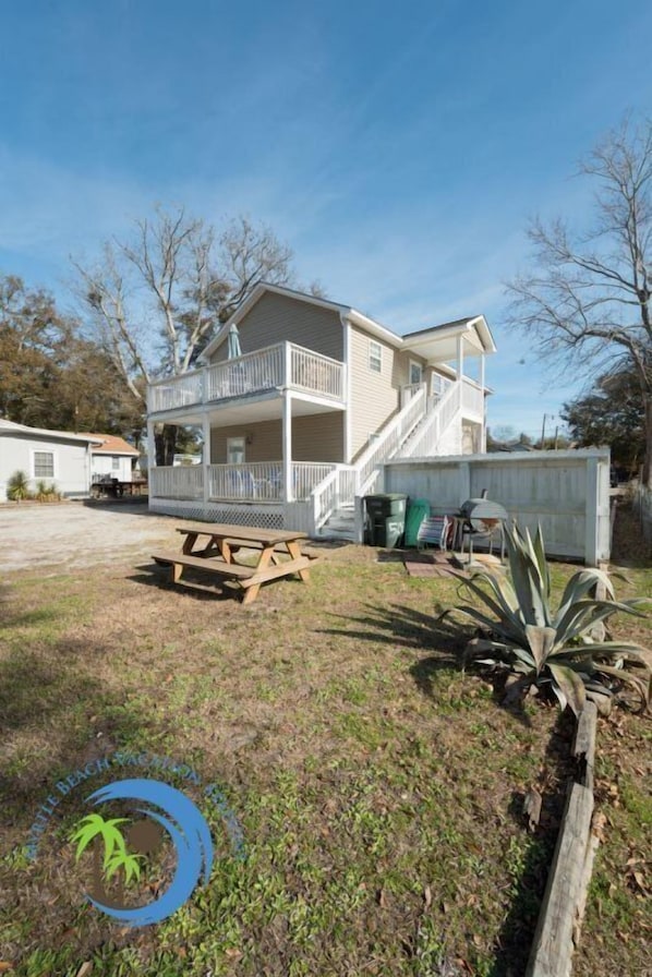 A two-story house with a balcony, a picnic table, and a wooden fence.
