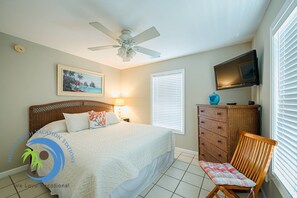 A bedroom with a bed, a ceiling fan, a TV, a dresser, and a chair.