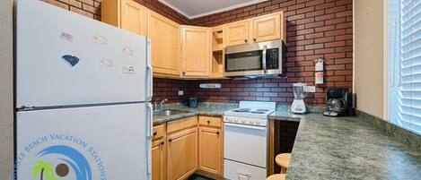 A compact kitchen with wooden cabinets, a refrigerator, a microwave, a stove, and a blender.