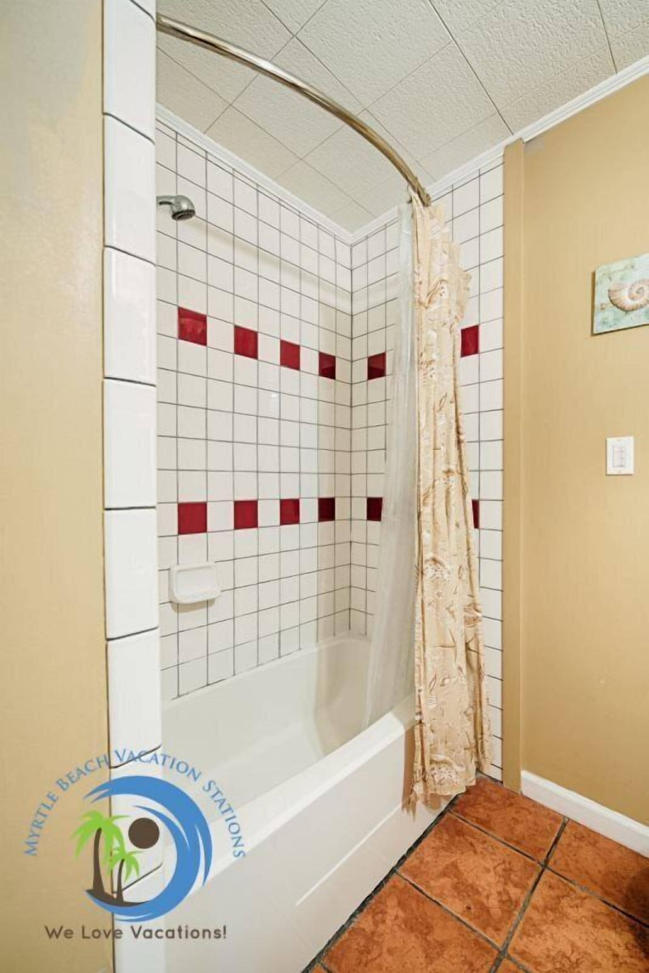A bathroom with a white bathtub, red square tiles, and a beige shower curtain.
