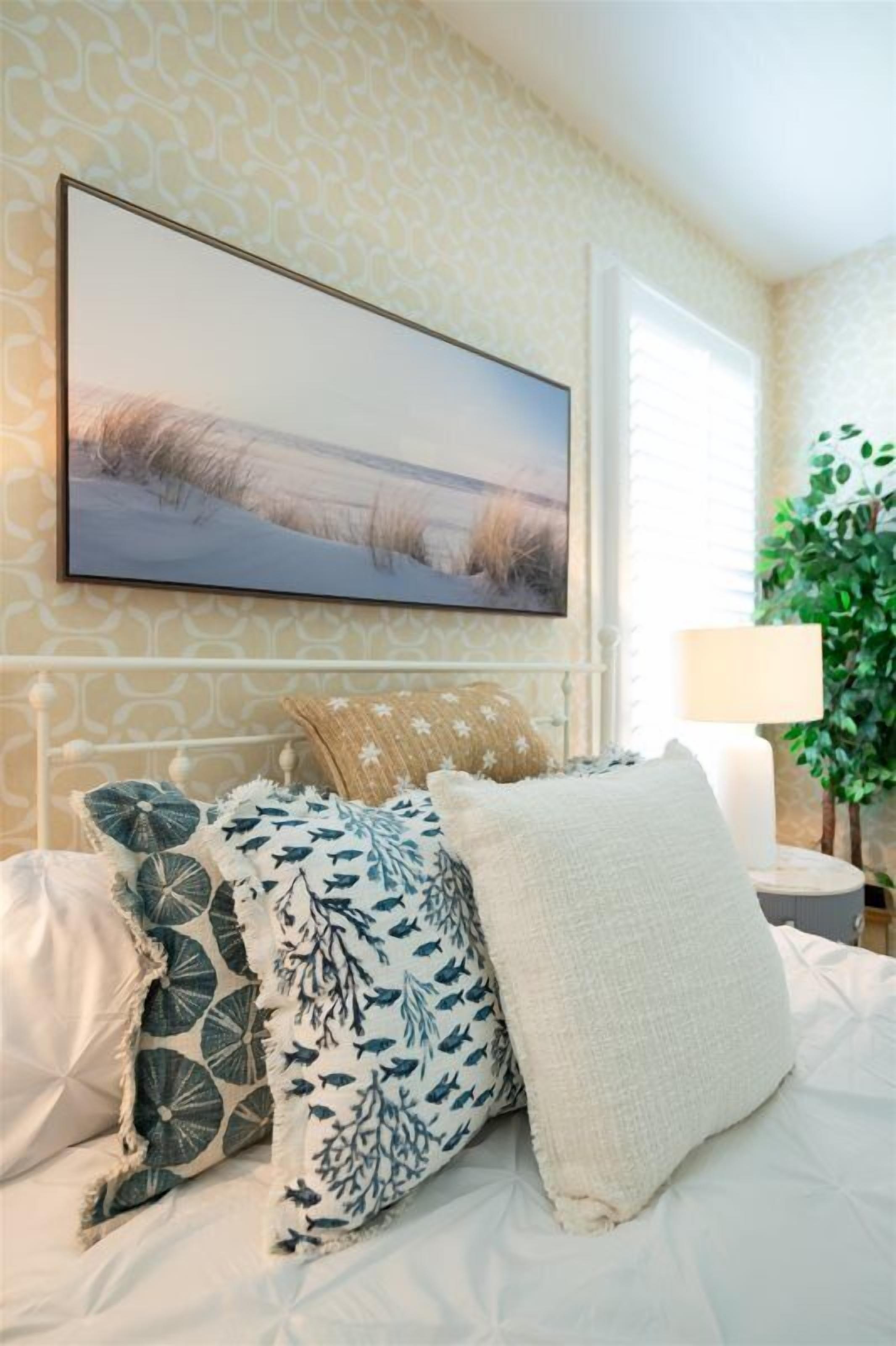 A bed with patterned pillows, a framed picture above it, and a bedside lamp.