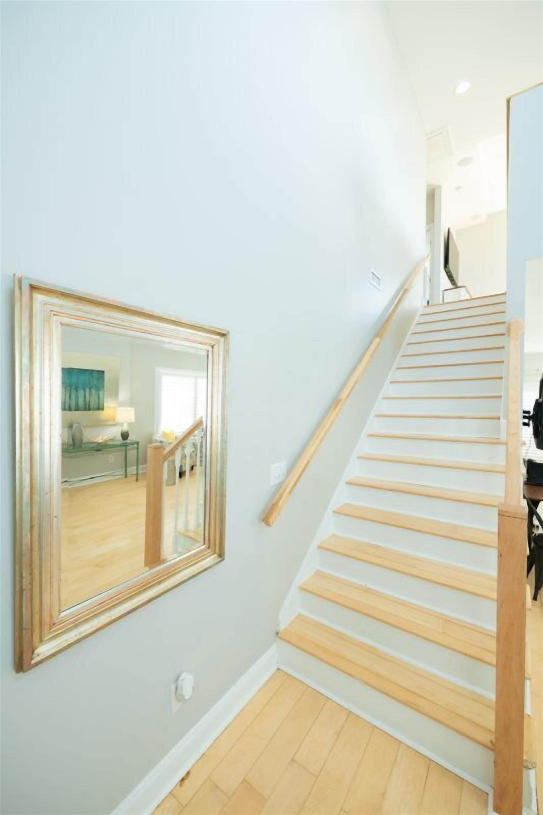 A staircase with wooden steps and a handrail, leading to a room with a large mirror on the wall.