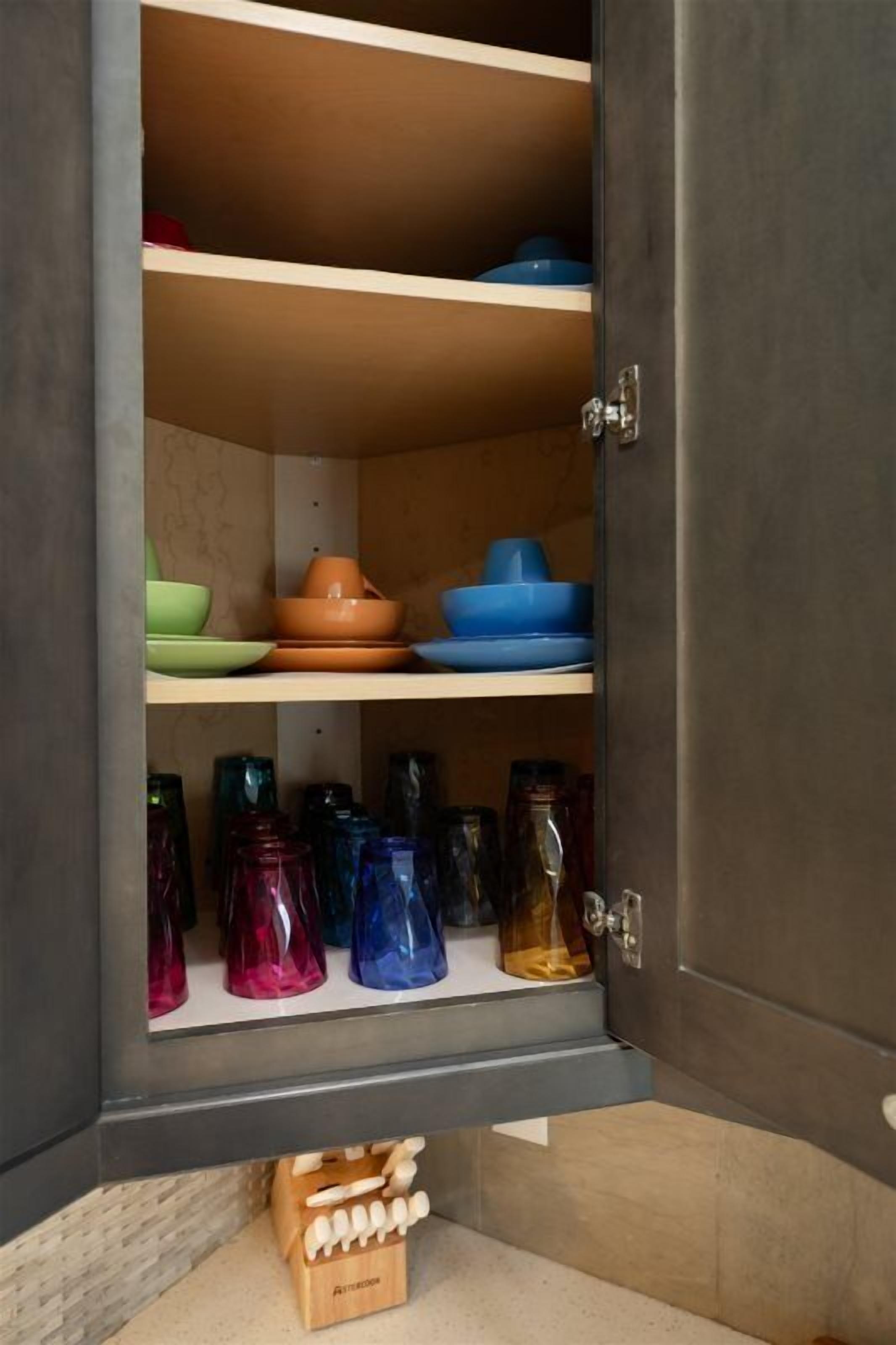A kitchen cabinet with shelves holding various colored bowls and glass jars.