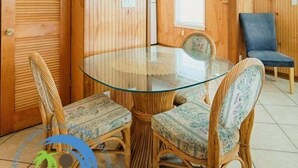 Quarto com mesa de vidro rodeada por cadeiras de vime, paredes de madeira e uma cadeira azul.