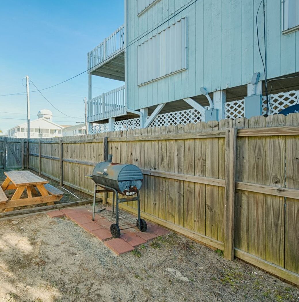 A backyard with a wooden fence, a barbecue grill, and a picnic table.