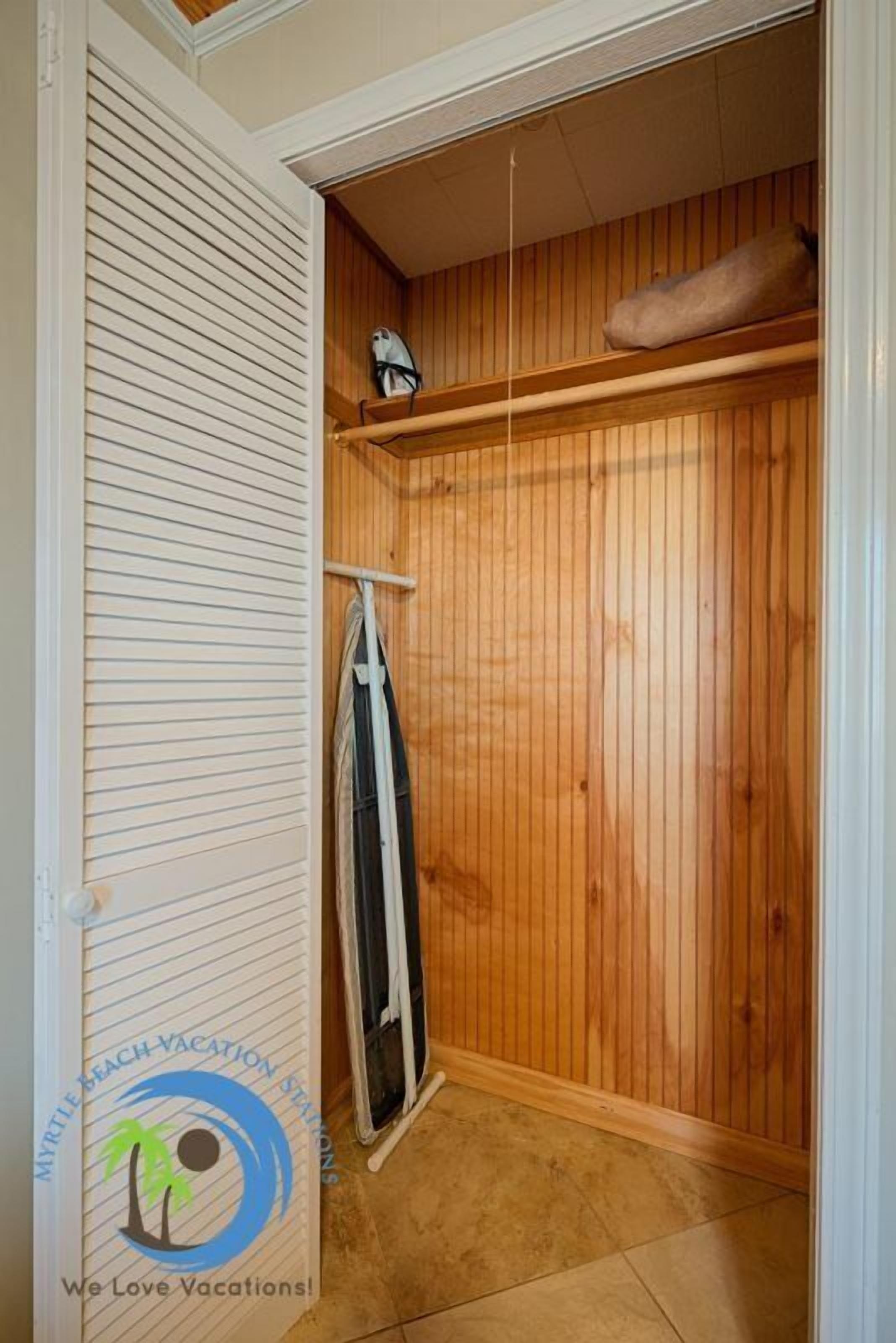 A wooden-paneled closet with a hanging rack and a folded item on top.