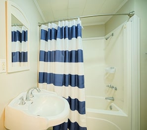 Bathroom features a bathtub and sink with a shower curtain and mirror.