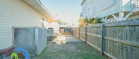 A backyard with a wooden fence, a grill, and a covered patio area.