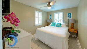 Une chambre à coucher avec un lit, deux tables de chevet, un ventilateur de plafond et une fenêtre.