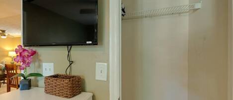 A room with a mounted flat-screen TV, a white cabinet, a wicker basket, and a small potted orchid.