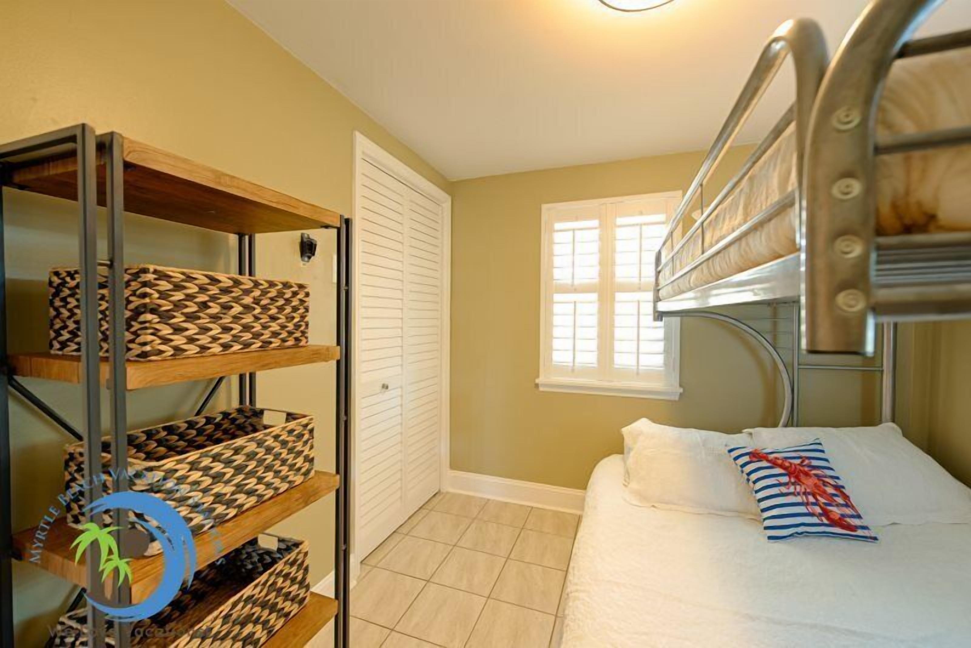 A compact bedroom with bunk beds, a built-in shelf unit, a window, and a door.