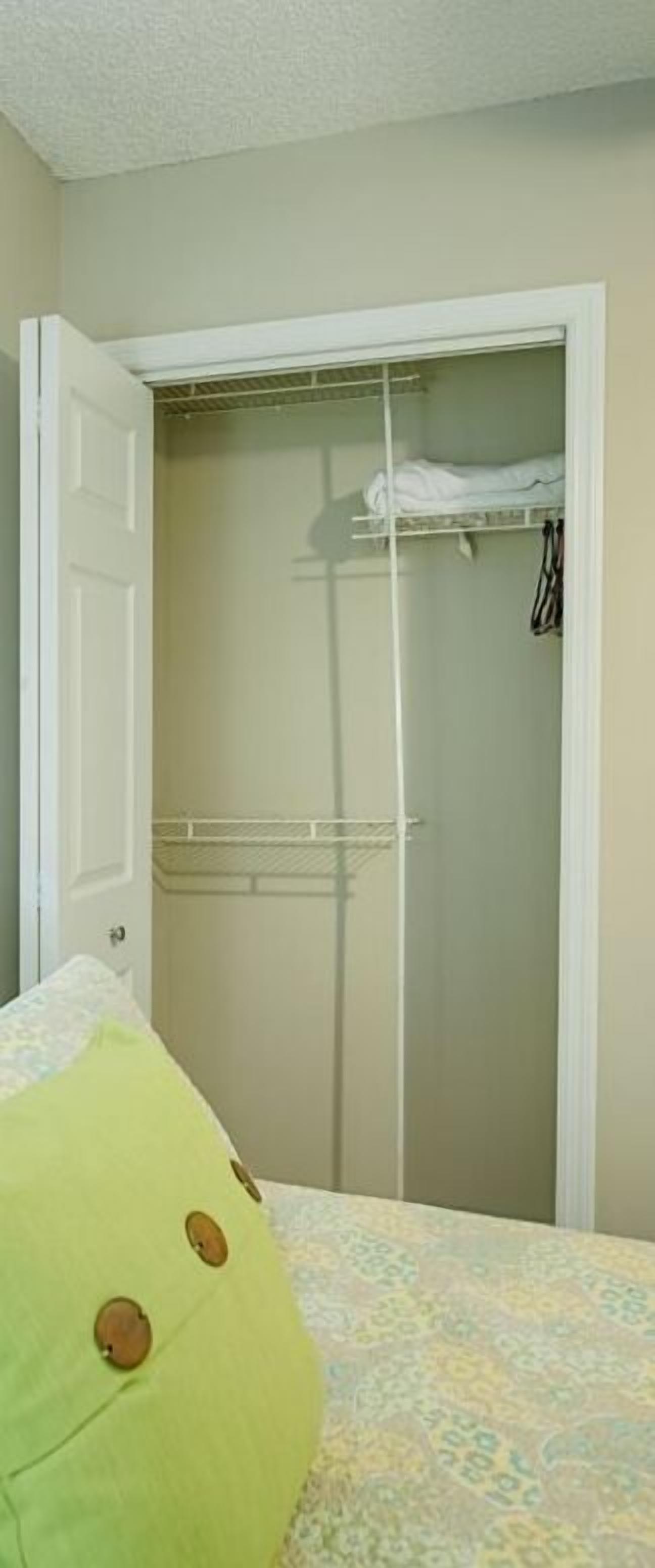 A bedroom with a bed, a green pillow, a wardrobe, and a hanging clothes rack.