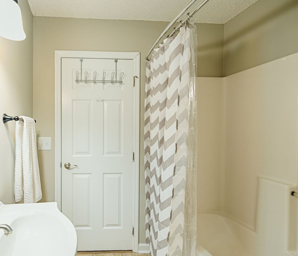 Une salle de bain avec une porte blanche, un rideau de douche et un porte-serviettes.