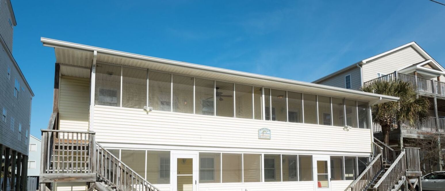 En toetagers bygning med en balkon på anden sal, en overdækket indgang og et synligt logo på facaden.