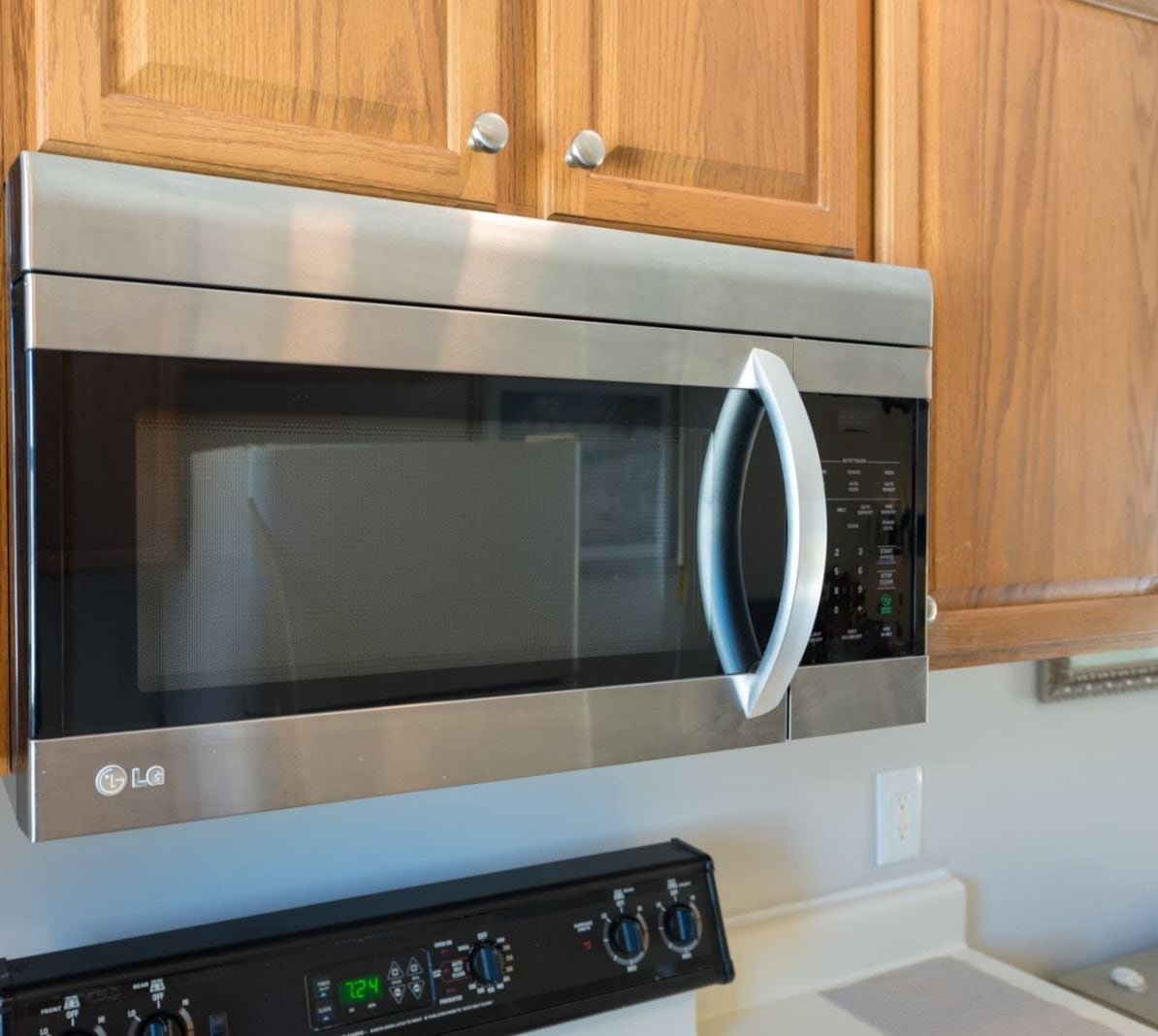 A stainless steel LG microwave oven with a digital control panel, installed in a kitchen with wooden cabinets.