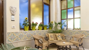 A room with a tiled wall, a window with frosted glass, and a wicker sofa with cushions. - Hotel Riva Del Sole (San Vito Lo Capo)