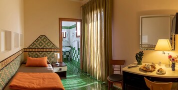 Habitación de hotel con cama, escritorio, silla, y baño visible a través de una puerta abierta, además de un televisor.