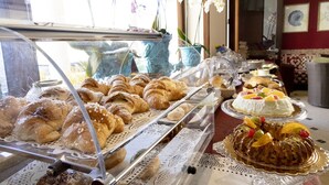 A bakery display with various pastries and cakes, including croissants and a bundt cake with fruit. - Hotel Riva Del Sole (San Vito Lo Capo)