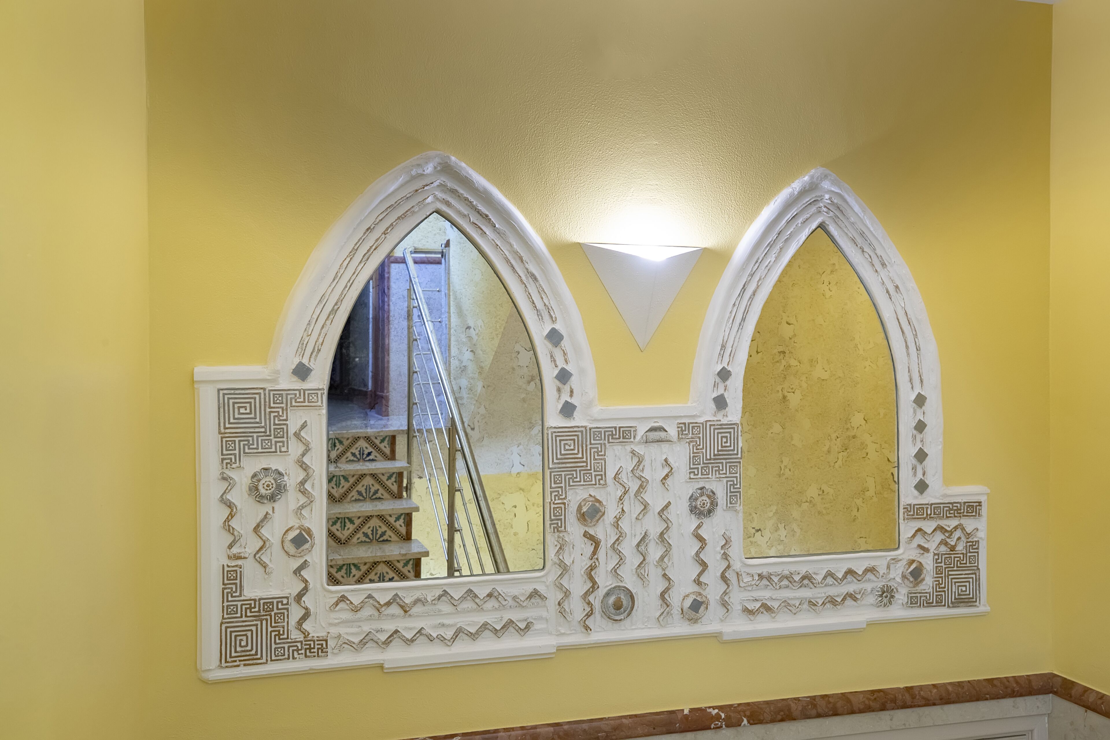 Un miroir orné de motifs blancs et dorés, placé devant un mur jaune.
