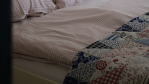 A bedroom with a white headboard, a bed with pink bedding, a blue lamp on a wooden side table, and a floral-patterned quilt. - Half-timbered house Dorothea up to 4 people (Stuer)