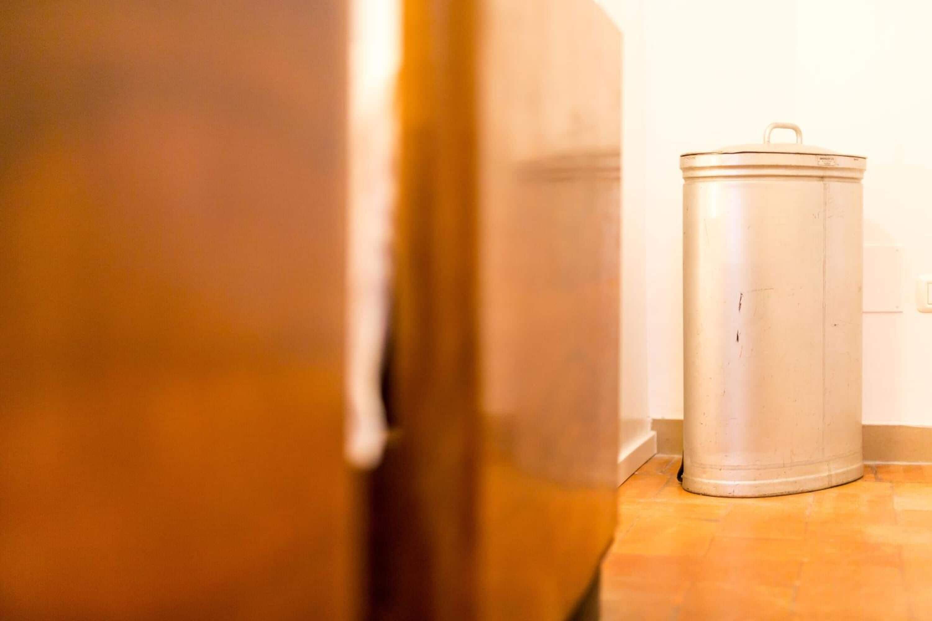A close-up of a white trash can next to a door.