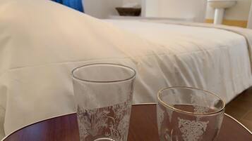 Zwei klare Glasbecher auf einem Holztisch in einem Hotelzimmer, im Hintergrund ein Bett.