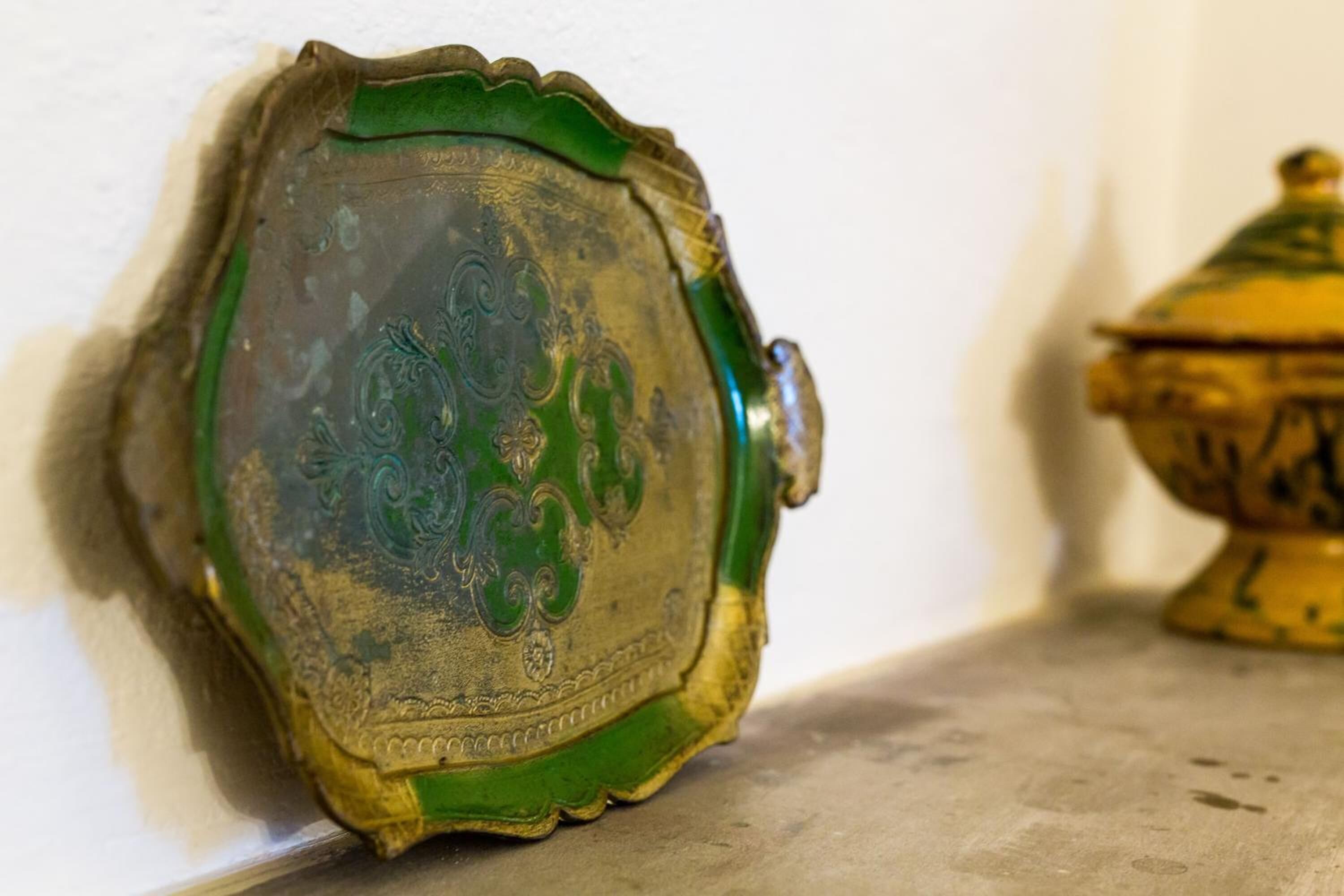 Eine gold- und smaragdgrüne dekorative Platte mit feinen Verzierungen, die an einer weißen Wand angebracht ist.