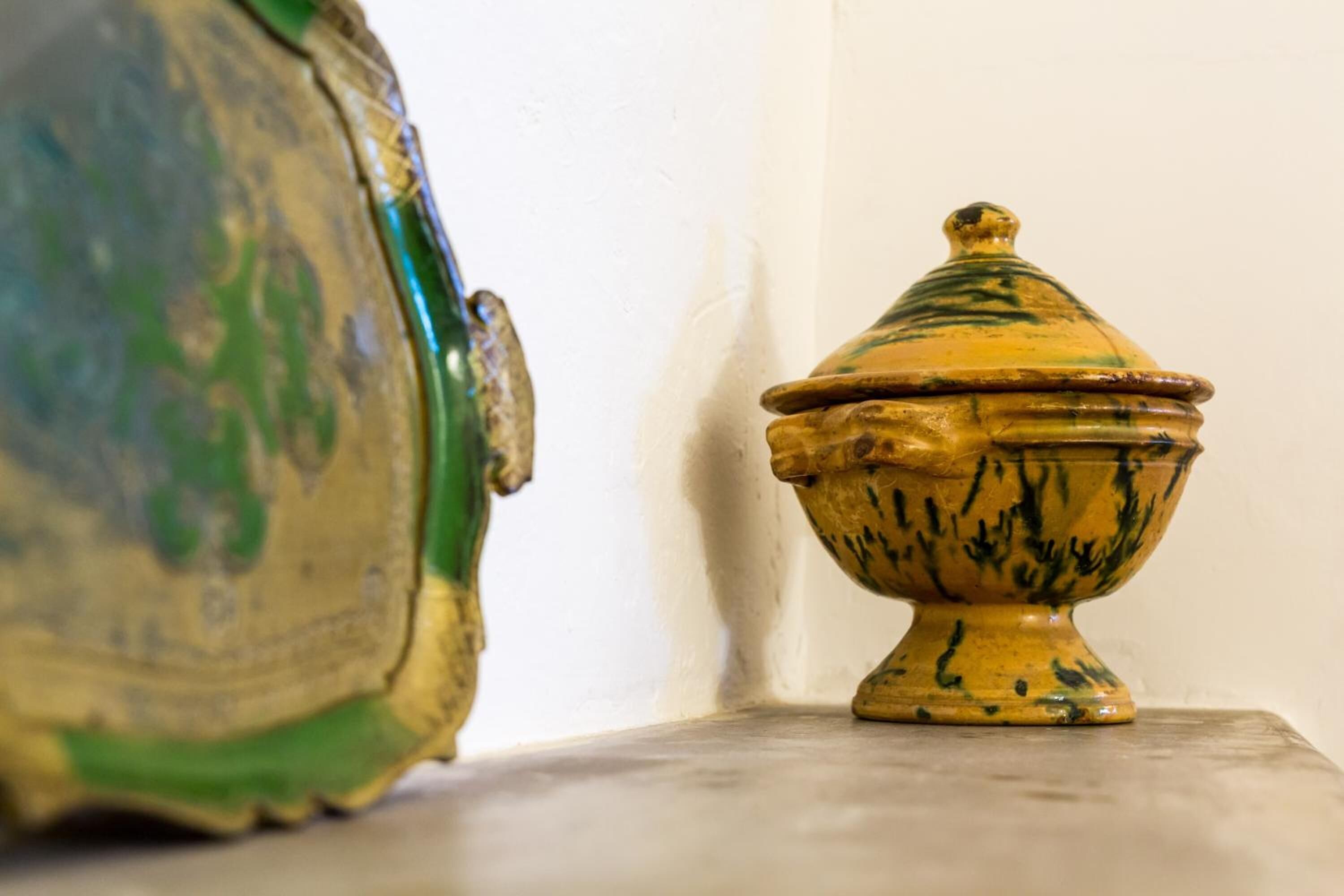 A ceramic pot with a lid on a table against a white wall.