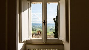 A window with a view of a rural landscape, including a building and trees. - Room En Suite Corte Assisi (Assisi)