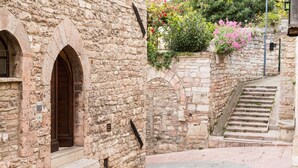 A stone building with a wooden door and steps leading up to a higher level. - Room En Suite Corte Assisi (Assisi)