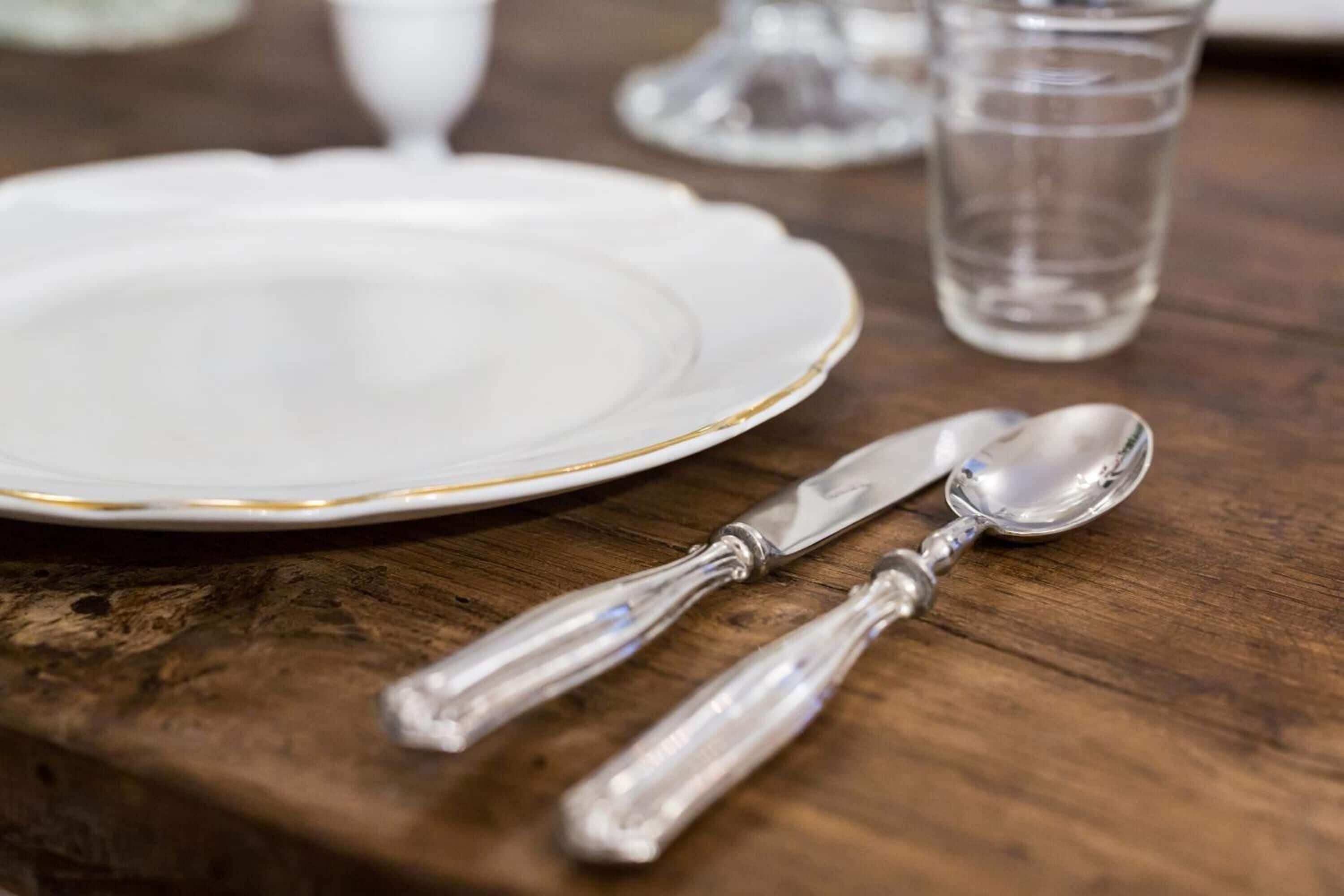 Une table en bois avec une assiette blanche, un couteau et une cuillère.