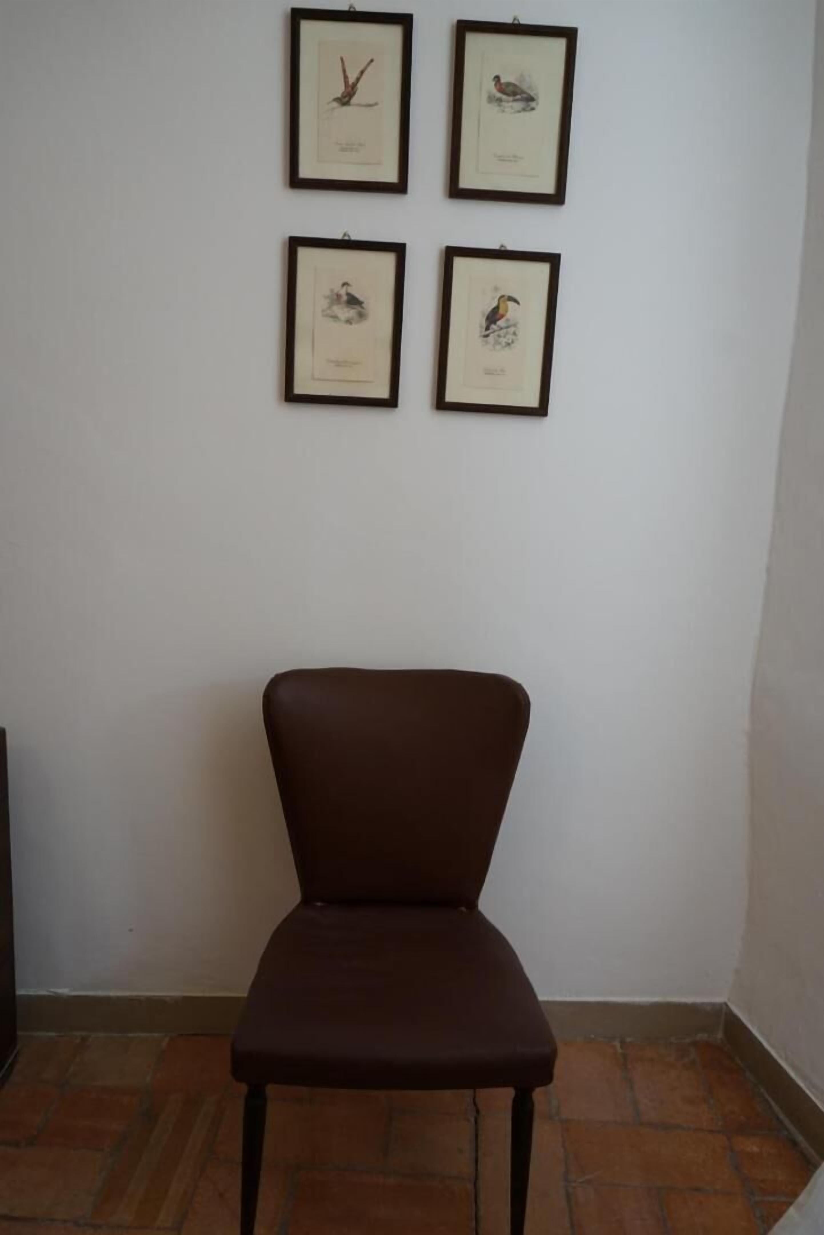 Quarto com uma cadeira marrom e quatro quadros na parede.