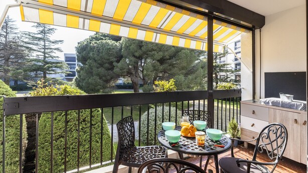 A balcony with a table, chairs, and a yellow-striped awning. - Les Embruns - Appt 2 ch avec parking (Saint-Cyprien)