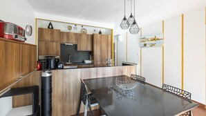 A modern kitchen with wooden cabinets, a black countertop, and a dining area with a black table and chairs. - Les Embruns - Appt 2 ch avec parking (Saint-Cyprien)