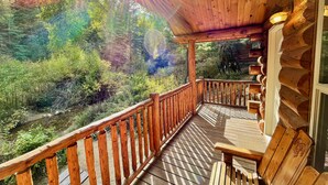 A wooden deck with a railing overlooking a forested area. - Secluded Creekside Cabin (Coaldale)