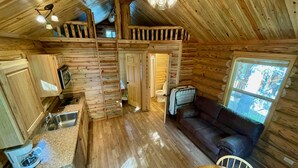A cabin interior with a kitchen, dining area, and a loft bedroom. - Secluded Creekside Cabin (Coaldale)