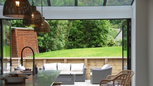 An outdoor patio with a dining area, seating, and a view of a lush garden.