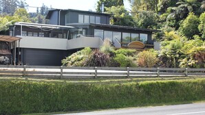 A modern two-story house with a garage, surrounded by lush greenery and a wooden fence.