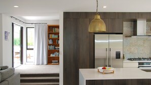 A modern kitchen with a large island, stainless steel appliances, and a wooden bookshelf.