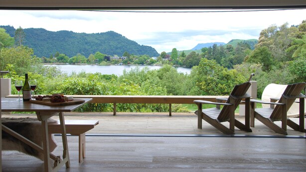 A wooden deck with a table and chairs overlooking a lake and forested hills.