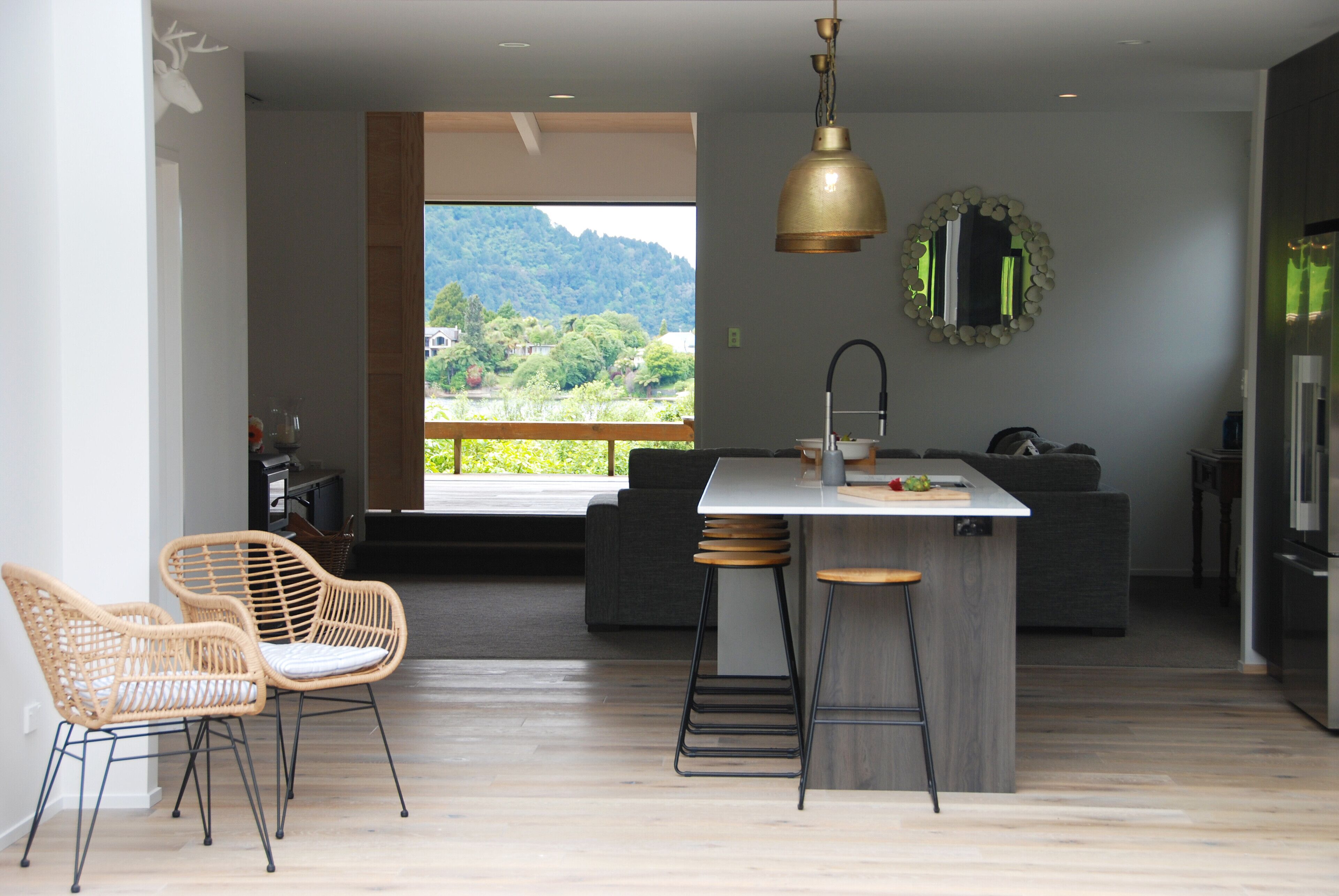 A modern kitchen with a central island, bar stools, and a large window offering a view of greenery.