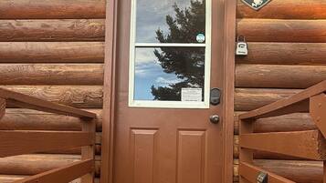 Une porte en bois avec une fenêtre, un panneau indiquant la présence d’un système de sécurité et un paillasson avec l’inscription « Bonjour ».