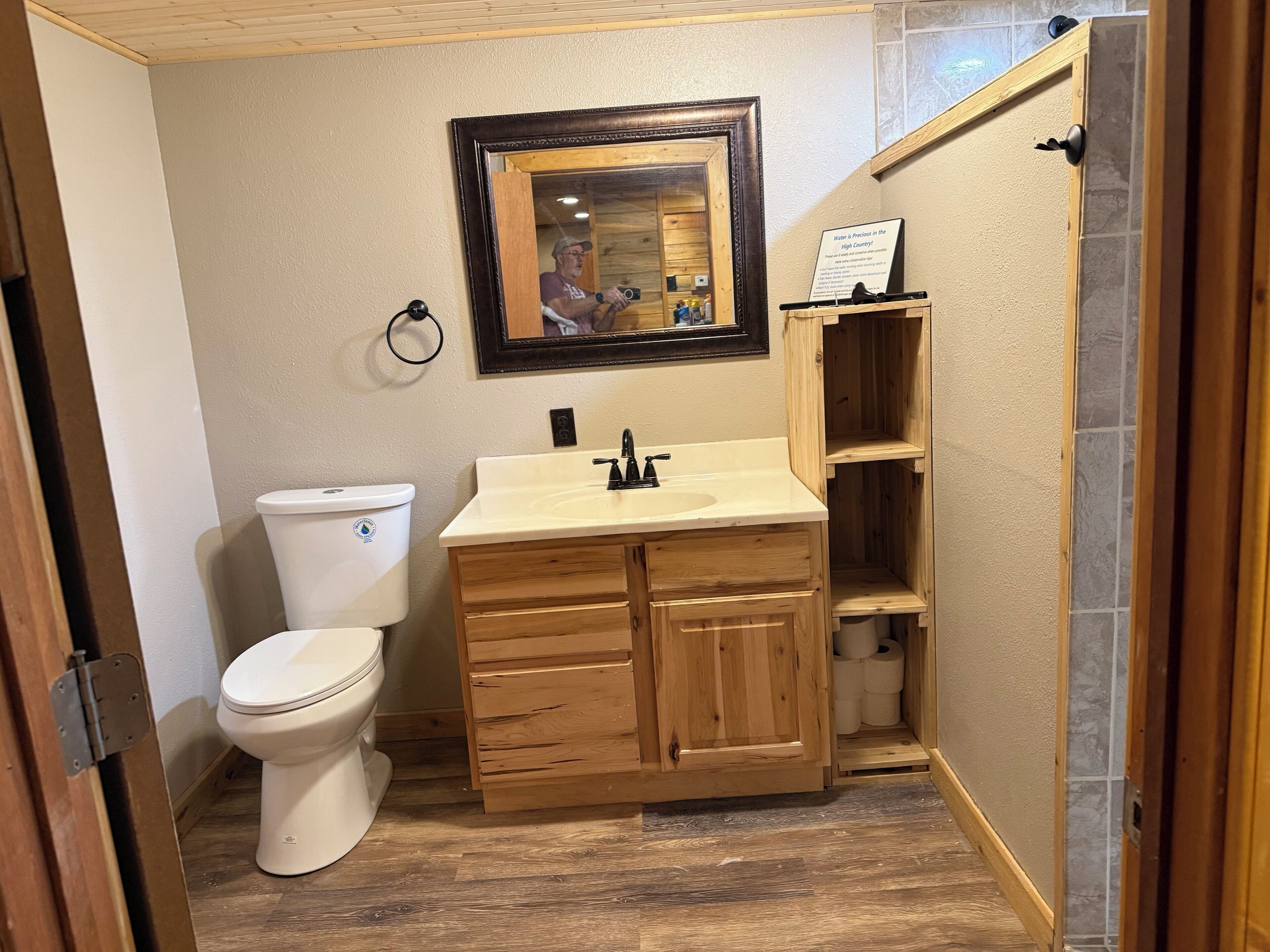 Een kleine badkamer met toilet, houten wastafelmeubel en spiegel.
