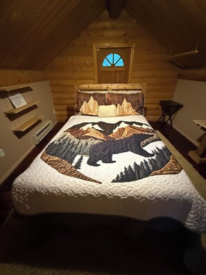 A log cabin bedroom with a bed featuring a mountain and bear quilt, a wooden headboard, a small window, and a wooden shelf. - Quiet, Cozy and Quaint Log Cabin Living! (Cotopaxi)