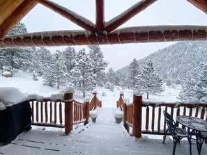 A snow-covered wooden deck with a view of a snowy mountain landscape. - Quiet, Cozy and Quaint Log Cabin Living! (Cotopaxi)