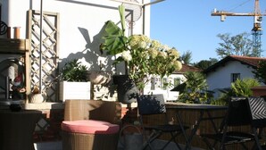 An outdoor patio with wicker furniture, a potted plant, and a view of a construction crane in the background. - Chambres d'Hotes Ene Gutizia (Ustaritz)